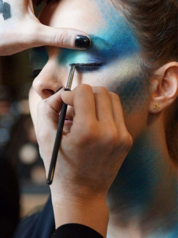 Mermaid Halloween makeup with blue shadow and scale shapes tapped across the temple and cheek of a woman