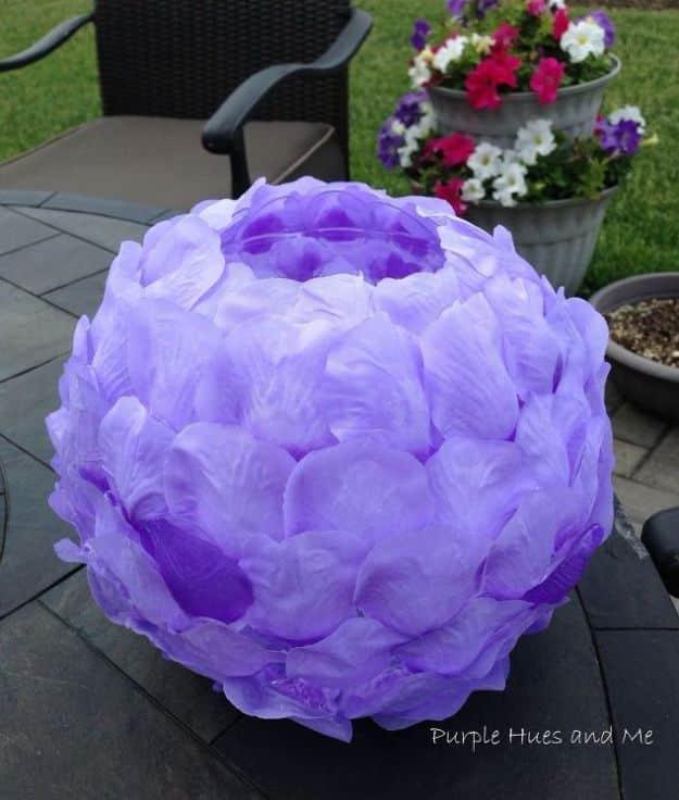 Rose petal luminary, a glass globe covered in lilac fabric petals lit from inside and sitting on a patio table