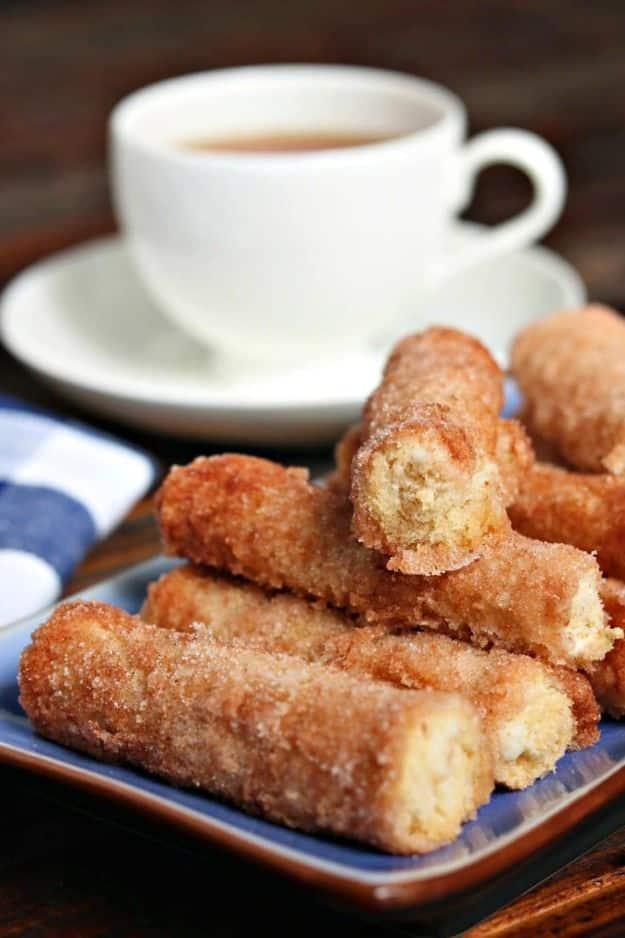 Baked cinnamon cream cheese roll ups stacked on a blue plate beside a white cup of tea on its saucer