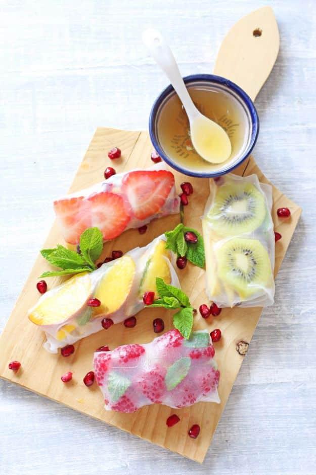 Fresh fruit spring rolls in rice paper with strawberry, kiwi and mint on a wooden board with honey dip