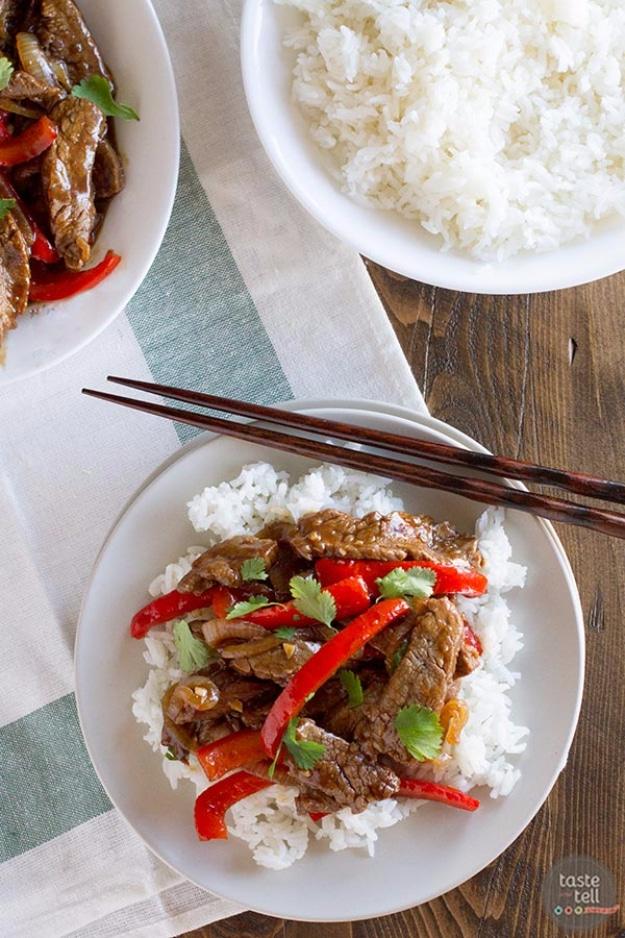 Steak stir fry with red pepper strips served over white rice on a plate with chopsticks laid beside it