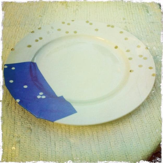 DIY confetti plates, a pale plate sprayed with gold confetti dots and a strip of punched blue painter's tape still stuck down