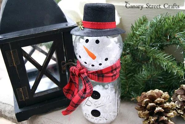 Mason jar snowman with a clear glass ornament head, hand painted face, fake snow inside and a scarf at the neck