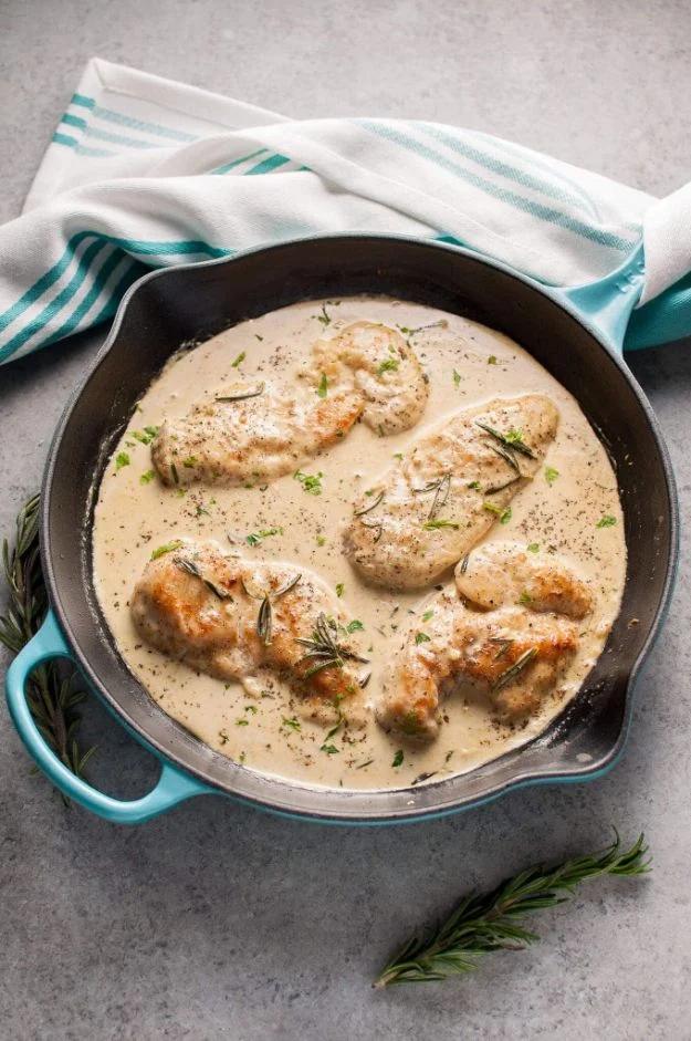 Creamy Dijon rosemary chicken cutlets in a pale sauce in a teal cast iron skillet with rosemary sprigs beside