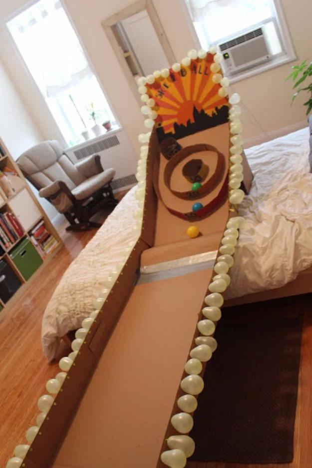 Cardboard craft skeeball ramp built from cardboard with a painted target ring and rows of balloon lights on a floor