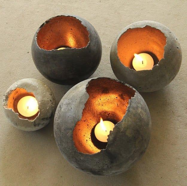 Hand blown concrete bowls, four round gray cement spheres with torn openings and lit tealights glowing orange inside