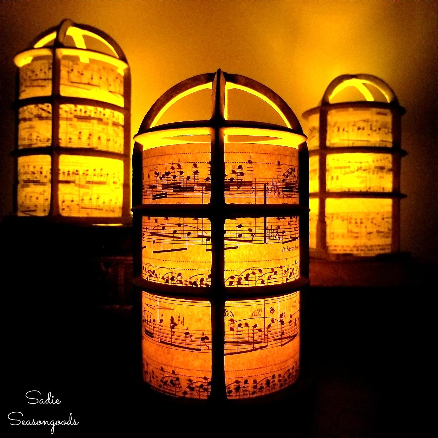 Three wire light bulb cages lined with vintage sheet music glowing amber from tea lights inside against a dark background