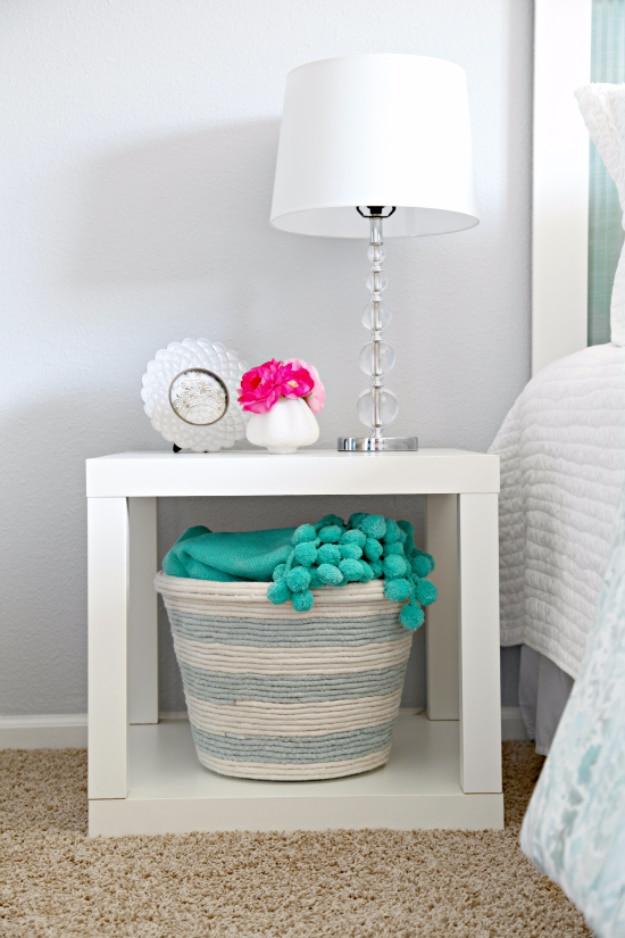 Cream and blue striped rope wrapped basket holding a teal blanket, sitting under a white bedside table