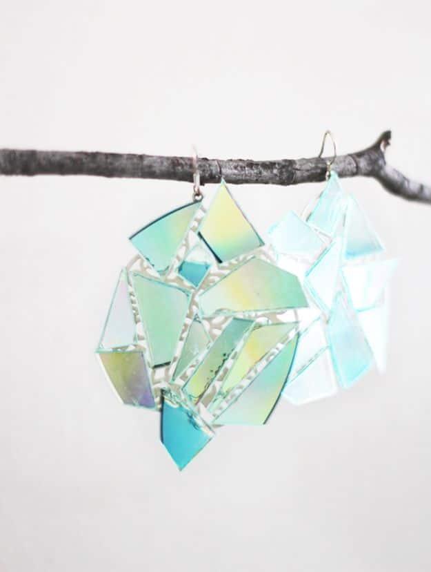 Pair of earrings made from cut pieces of an old CD in pale green and blue iridescent shards, hanging from a bare branch
