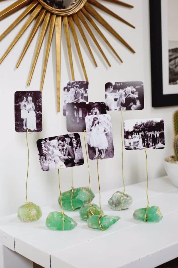 Cluster of green mineral chunks wrapped in gold wire holding small black and white photos upright on a white console table