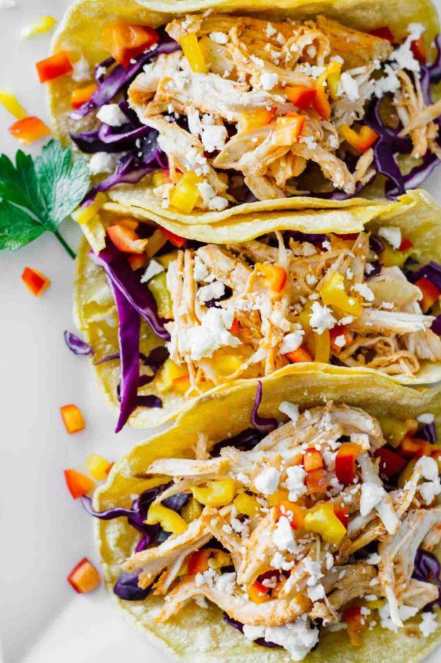Healthy sriracha shredded chicken tacos in corn tortillas with red cabbage, bell pepper, feta and cilantro