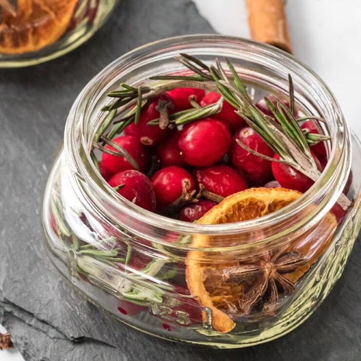 Glass jar layered with dried orange slices, cranberries, cinnamon and cloves for slow cooker holiday potpourri