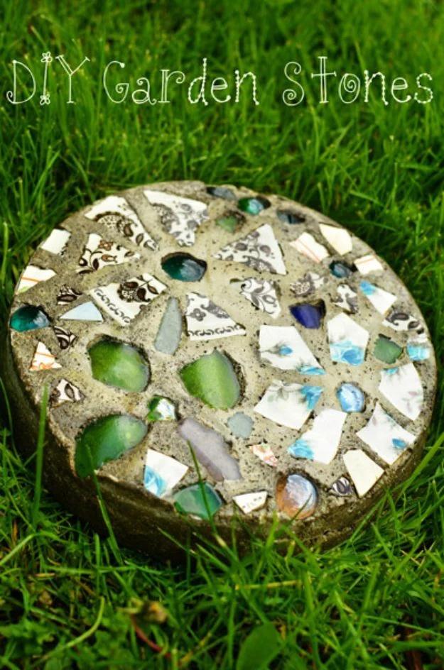 Round concrete garden stone studded with colored glass gems and broken china, set down into green grass