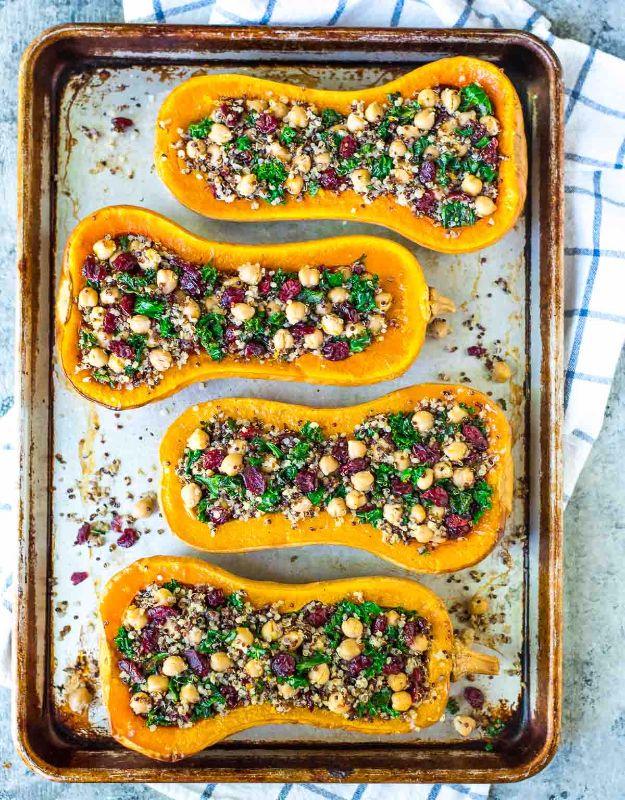 Four butternut squash halves on a rimmed baking sheet stuffed with quinoa, chickpeas, kale and cranberries