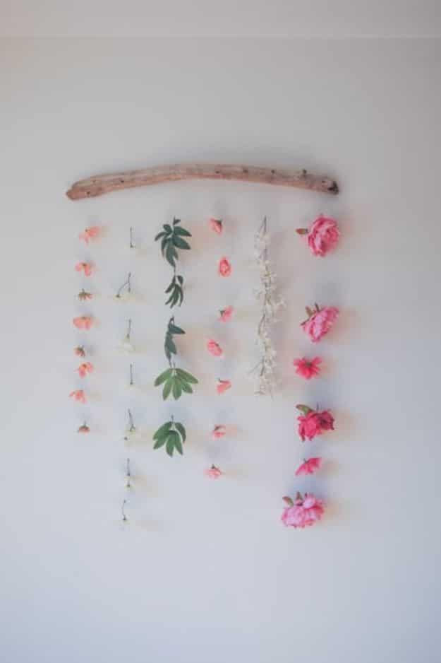 Faux pink flowers and green leaves hanging in rows from a driftwood branch against a plain white wall