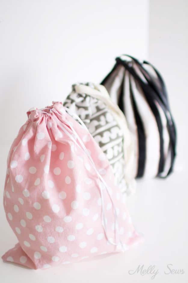 Drawstring bags sewn in pink polka dot, cream print and black stripe cotton, gathered shut with cream cord on a white surface