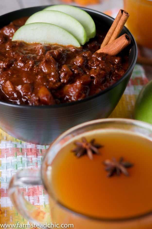 Apple cider chili in a black bowl garnished with apple slices and a cinnamon stick beside a mug of cider