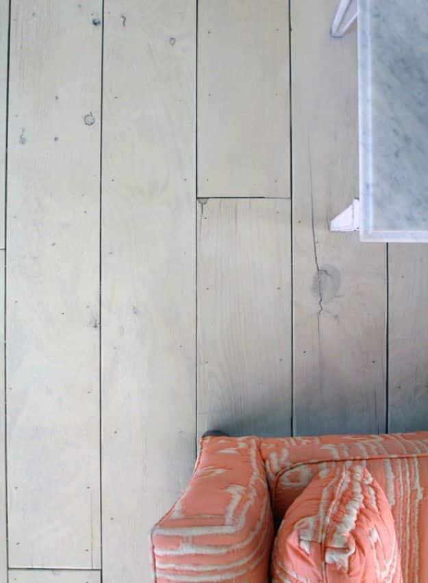 DIY wide plank floors, pale whitewashed plywood planks with thin dark seams beside a coral ikat floor cushion