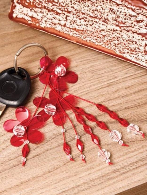 Red flower key chain made from painted plastic bottle petals and clear beads on a key ring, on a wooden table