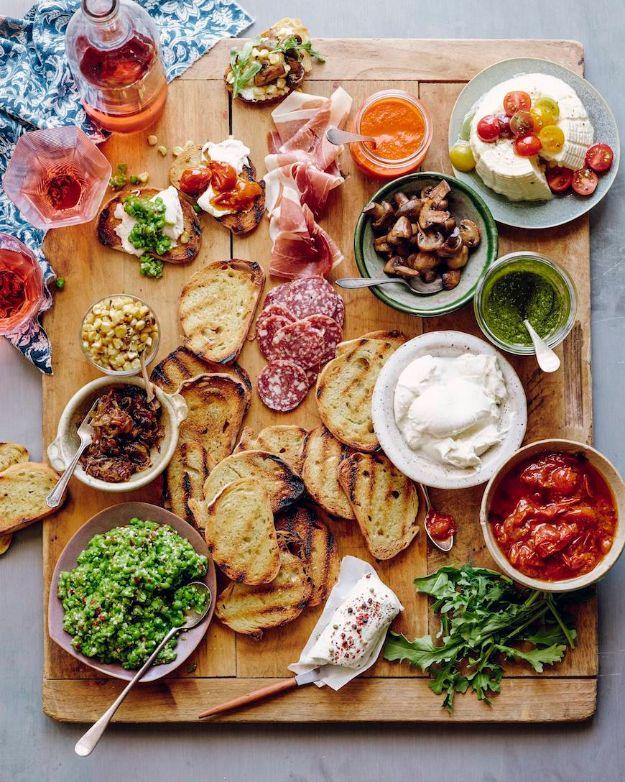 Bruschetta bar on a wooden board with grilled bread slices, bowls of tomato and pesto, salami and soft cheeses