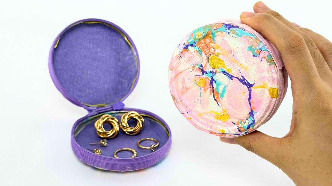 Nail polish marbled jewelry purse, a hand holding a round marbled pink case open to a purple lined ring holder