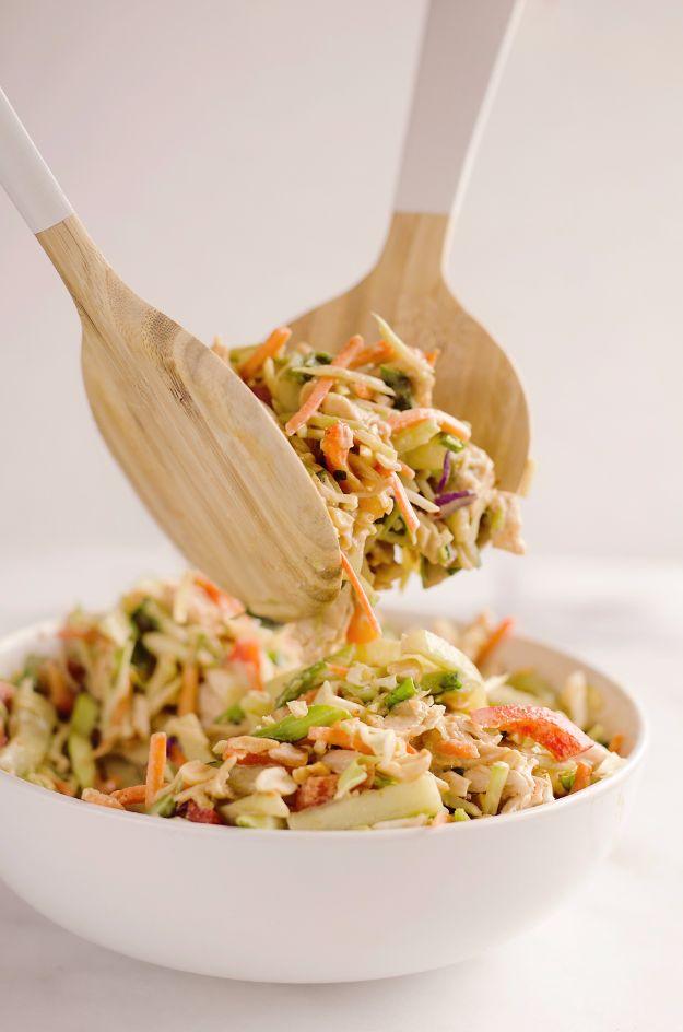 Thai peanut chicken crunch slaw salad being lifted from a large white bowl with a pair of wooden salad servers