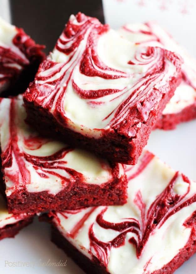 Red velvet swirl brownies piled on a white surface with bright red bases and white cream cheese swirls