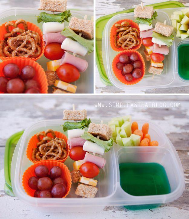 Sandwich kabobs in bento boxes with cubes of ham, cheese, tomato, pretzels and grapes in silicone cups