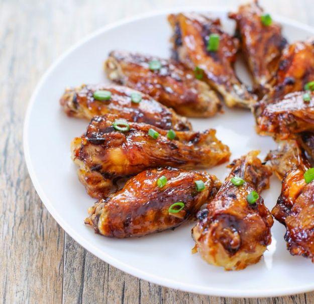 Coca Cola bourbon chicken wings, lacquered mahogany wings scattered with sliced scallion on a white plate on weathered wood