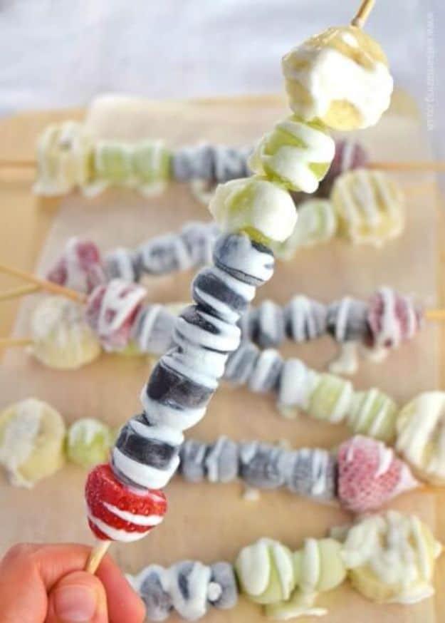 Frozen rainbow fruit kebabs on skewers with strawberries, grapes, blueberries and banana, drizzled with yogurt and honey