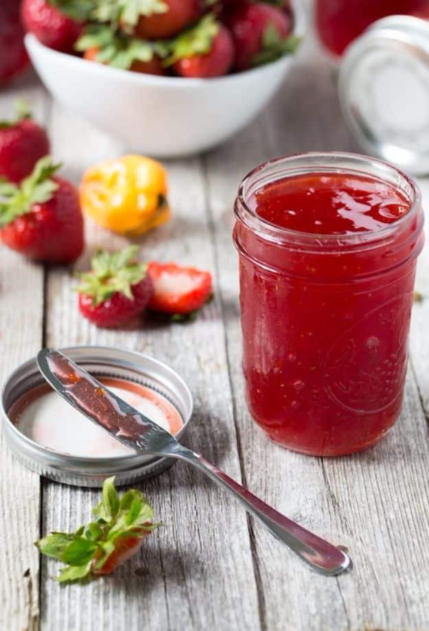 Strawberry habanero jam in twelve ounce jars, bright red with minced habanero, beside fresh strawberries