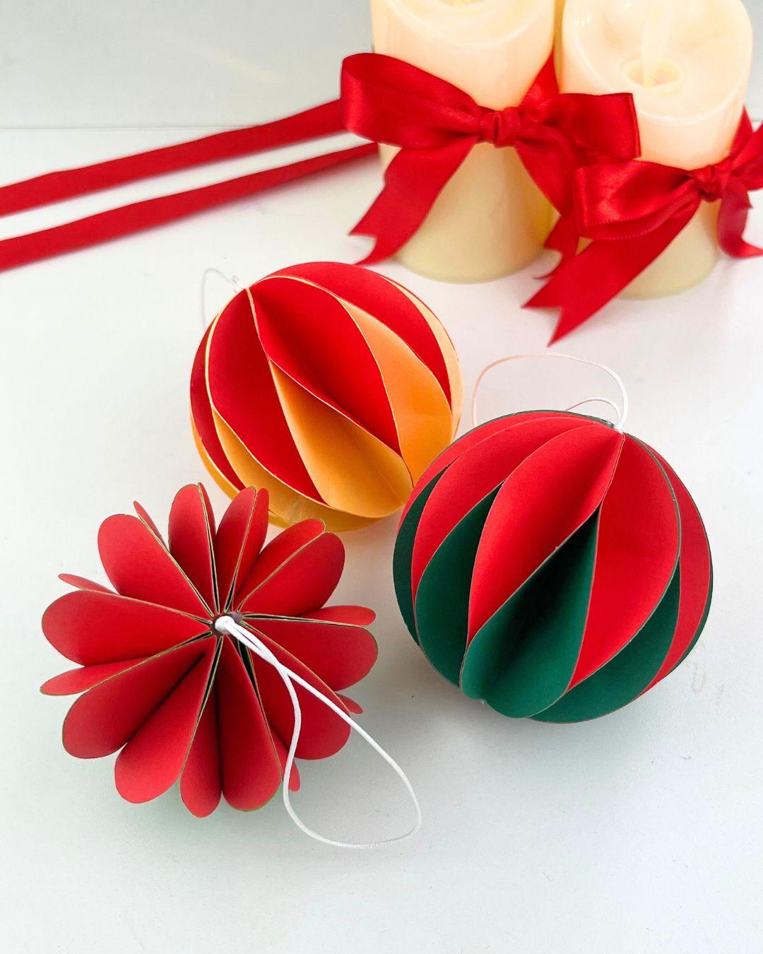 DIY Ornament Ideas - two striped paper ball ornaments beside a red one left open flat into a rosette shape tied with white string