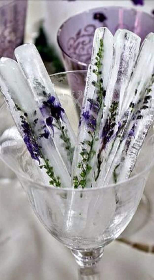 Tall clear ice sticks with lavender flowers and tiny roses frozen inside, standing in a cut glass coupe