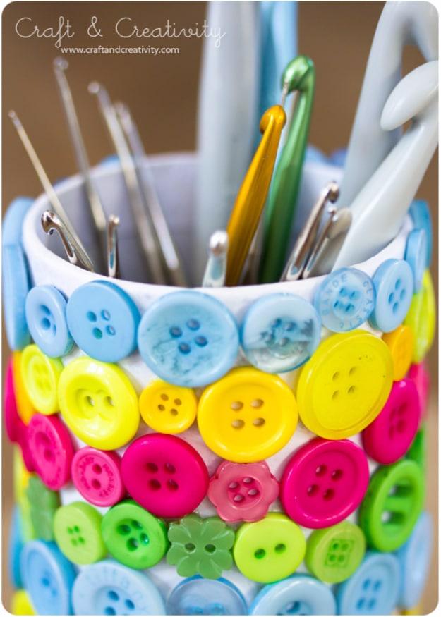 Button crafting tools holder, a tin covered in bands of blue yellow pink and green buttons holding crochet hooks
