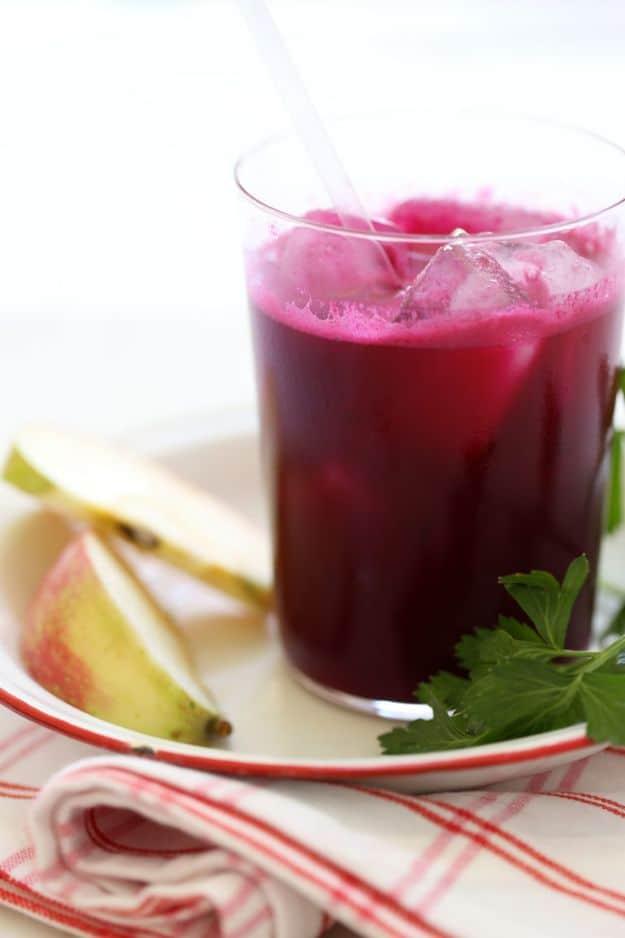 Beet ginger detox juice over ice with a straw beside sliced apple and parsley on a red striped napkin