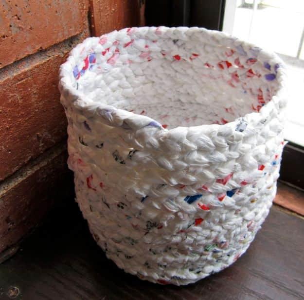 Woven basket coiled from braided white plastic bag strips flecked with red and blue print, sitting on a windowsill