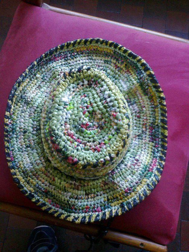 Wide brimmed sun hat crocheted from green and yellow plastic bag plarn, resting crown up on a pink cushion