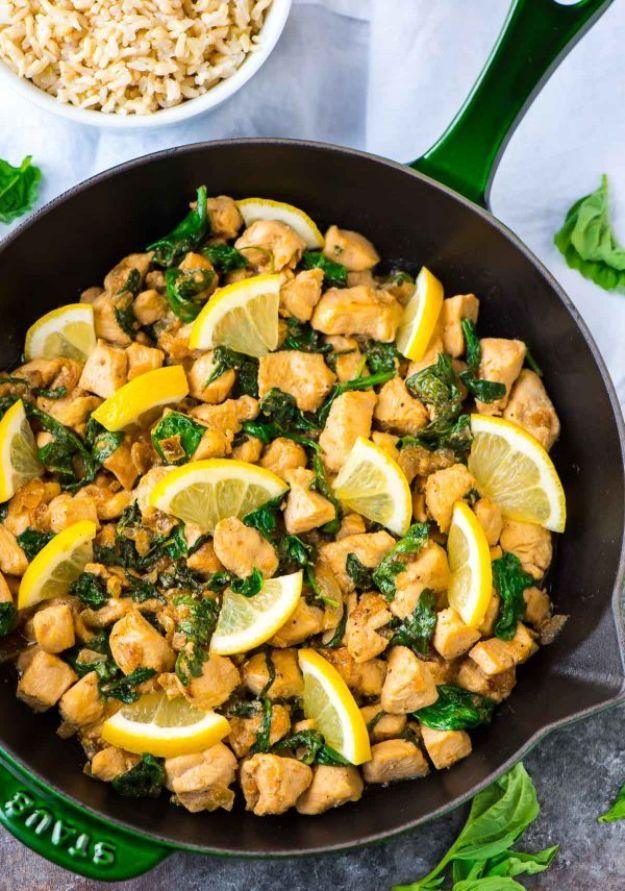 Lemon basil chicken in a green handled skillet with chicken pieces, wilted greens, basil and lemon slices