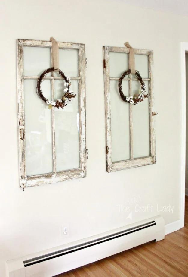 Two small grapevine wreaths with cotton bolls hung on old white window frames against a pale cream wall