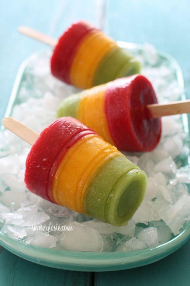Frozen mango kiwi raspberry pops layered in green, gold and red fruit puree stripes on sticks, a layered fruit popsicle