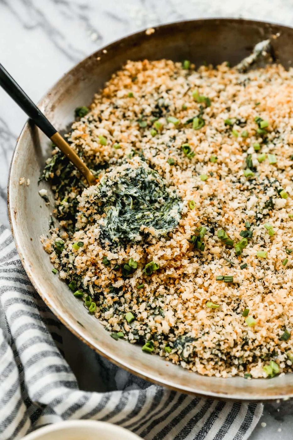 Spinach parmesan casserole under a thick golden panko crust in a skillet with a serving spoon resting in it