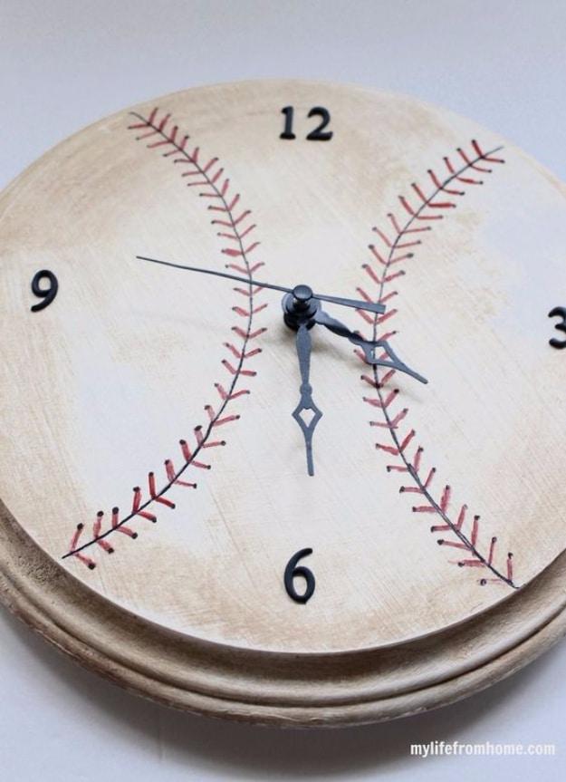 Round wooden clock painted as an aged baseball with red stitching, navy numbers and navy hands on a pale surface
