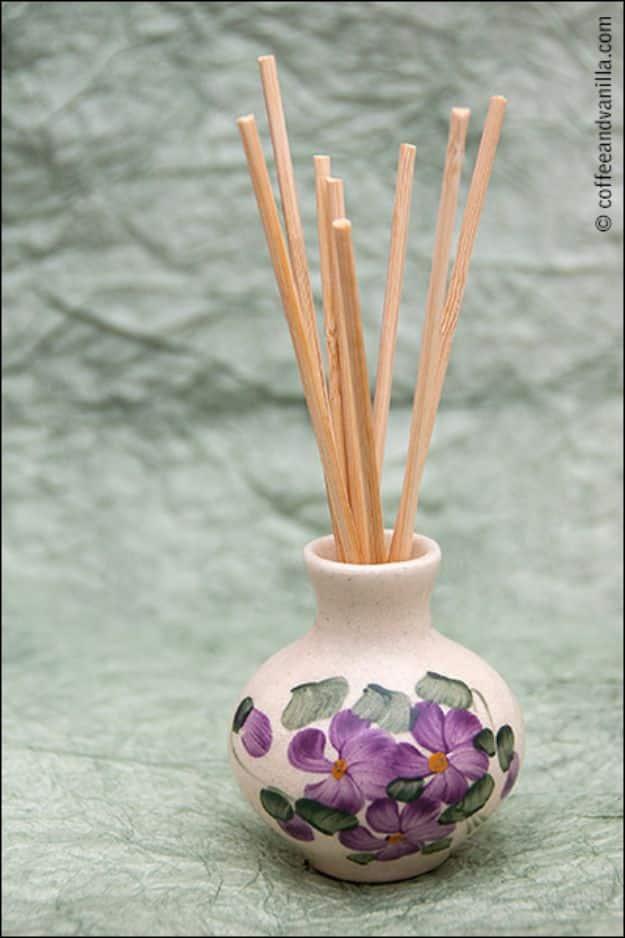 Painted ceramic bottle with violet flowers holding a bunch of natural diffuser reeds against a gray background