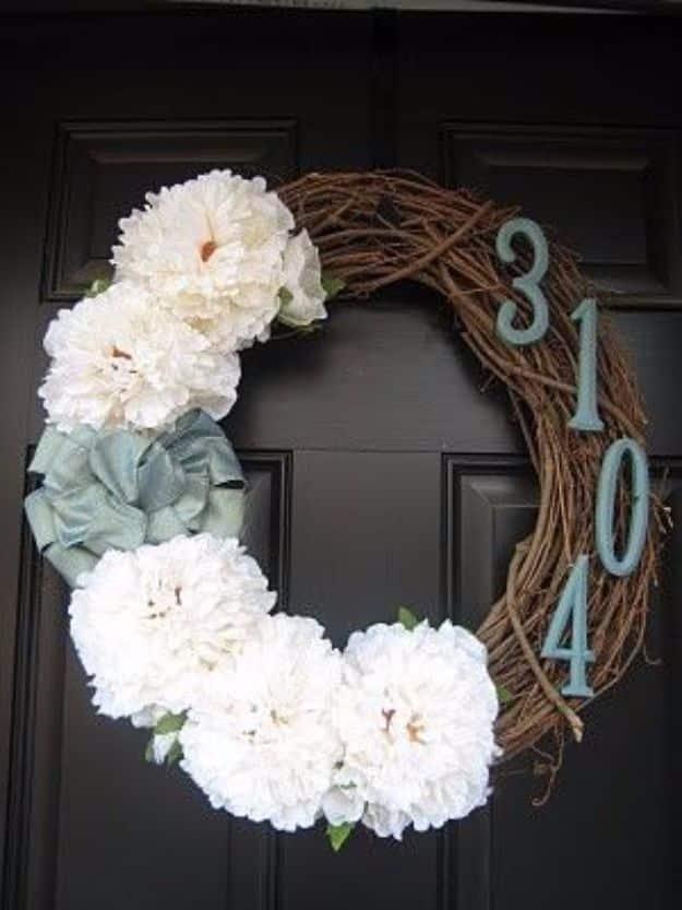 Twig wreath with white felt flowers and blue metal house numbers set into the twigs, on a black door