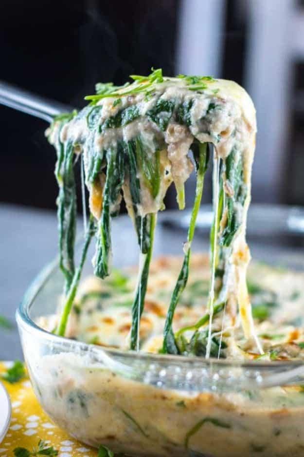Cheesy low carb creamed spinach being lifted with a fork from a glass baking dish in long cheesy strands