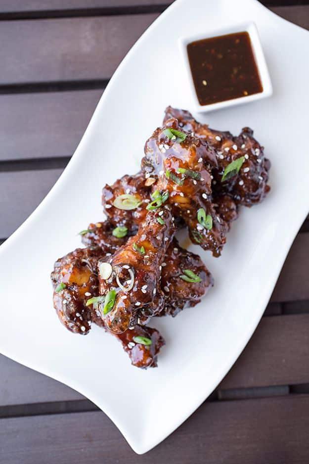 Korean BBQ style Coca Cola hot wings, dark glossy drumettes on a white platter with scallion, sesame and dipping sauce