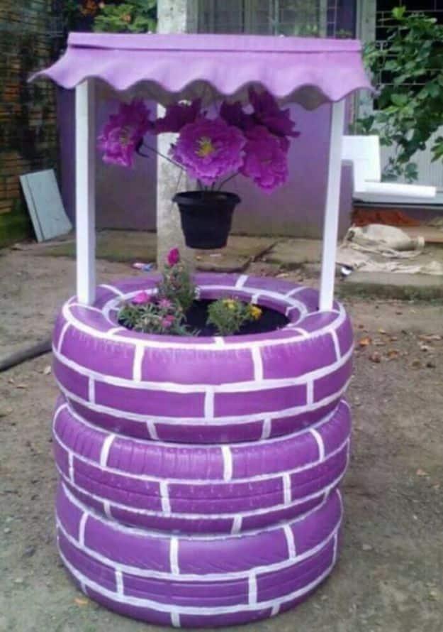 Three purple painted tires stacked as a wishing well planter with white brick lines and a scalloped purple roof