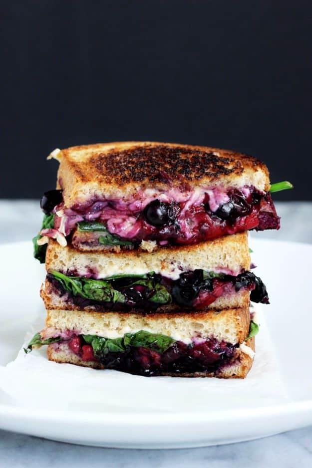Stacked halves of vegan grilled cheese with melted cheese, balsamic berries and fresh spinach inside