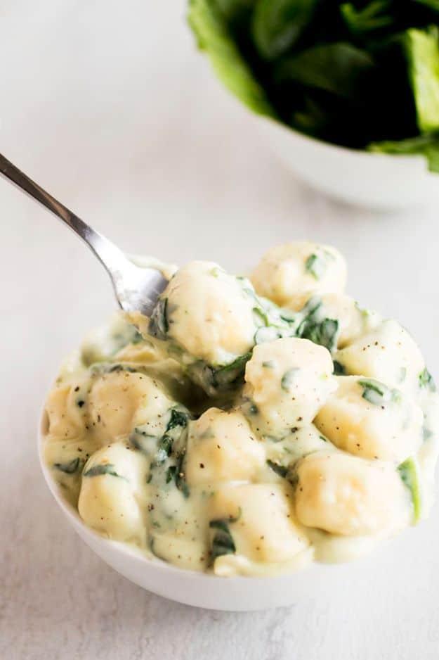 Parmesan spinach gnocchi in a creamy sauce in a white bowl with a spoon and fresh spinach leaves behind