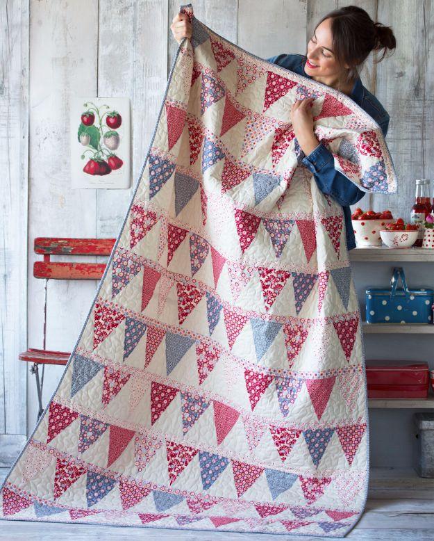 Candy bloom quilt held up by a maker, rows of red and blue triangle bunting on cream with pale print sashing